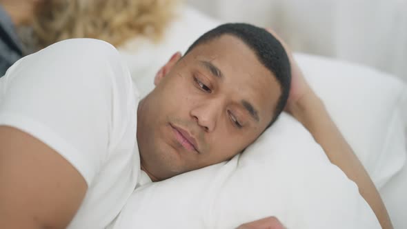 Closeup Portrait of Sad Young Handsome African American Man Lying in White Bed Looking Over Shoulder alt