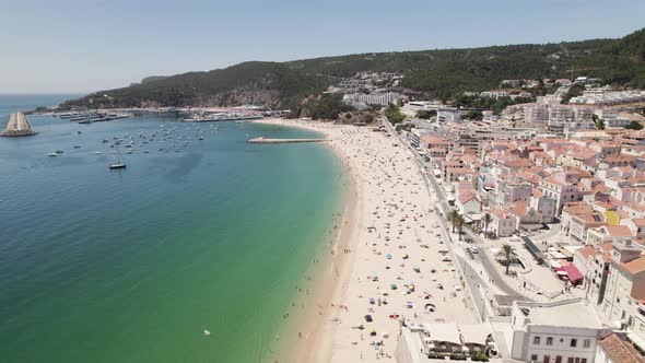 Aerial backwards view of long and beautiful beach with its bay in Sesimbra. Portugal. Real time alt