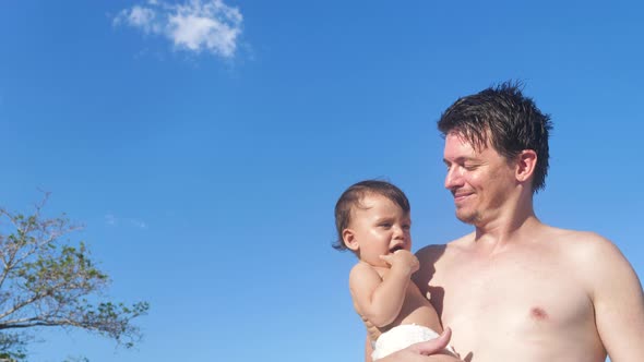 A Happy Young Father Carrying a Baby with Blue Sky and Coconut Trees Background