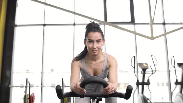 Portrait of a Beautiful Young Brunette Woman Doing Cardio on a Exercise Bike at Gym