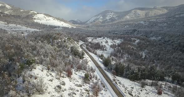 drone view of a completely snowy valley that is crossed by a road. alt