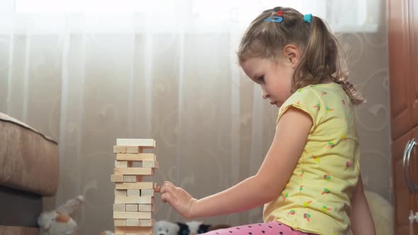 Curly-haired, blonde four-year-old girl is playing jenga game alt