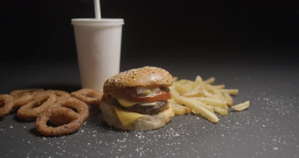 Fast food menu tracking shot in studio. Hamburger with french fries, onion rings and soda drink.