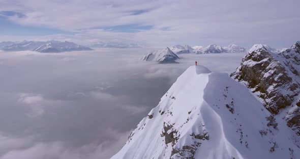 Aerial drone view of a mountain climber skier on the peak summit top of a snow covered mountain. alt