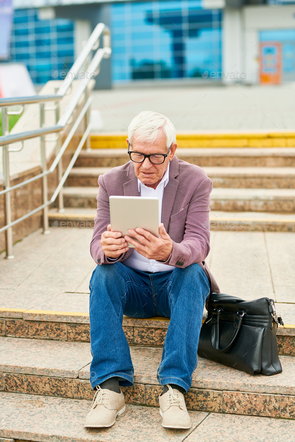 Aged entrepreneur with tablet on steps