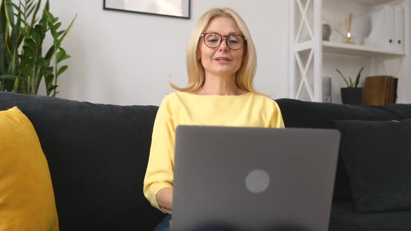 Confident 50s Middleage Female Teacher Using Laptop for Virtual Connection Sitting on the Sofa