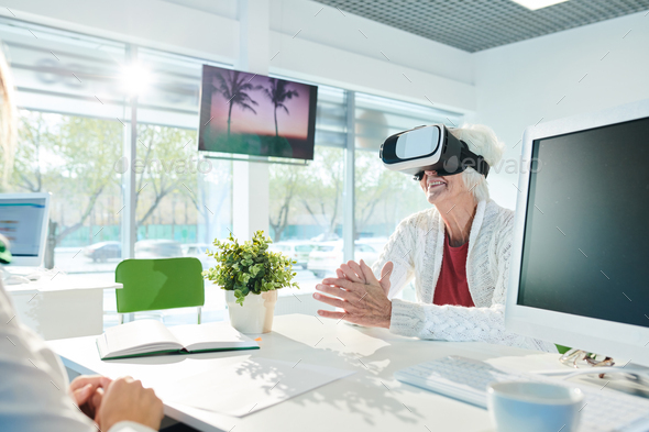 Happy senior lady in VR simulator enjoying virtual tour