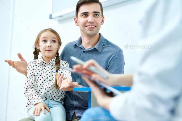 Lovely girl with young dad listening to doctor - Stock Photo - Images