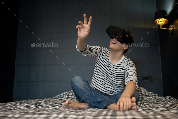 Smiling male sitting on bed using VR glasses