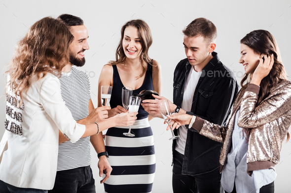 Girls and guys dressed in stylish casual clothes stand together and smile. Guy is pouring champagne
