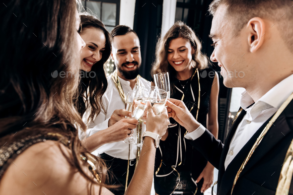 Company of happy friends dressed in stylish elegant clothes stand together and clink glasses with
