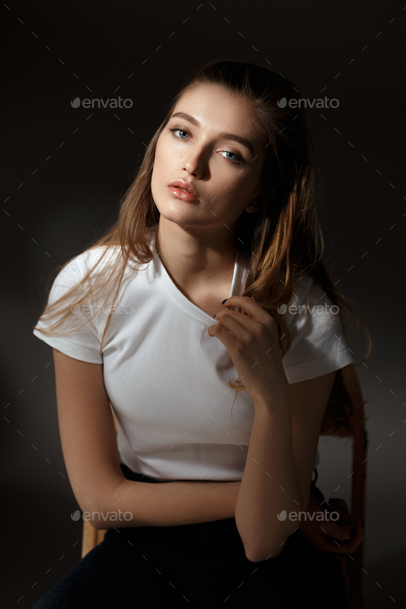 Trendy girl in white shirt posing on white wall backdrop. Brunette