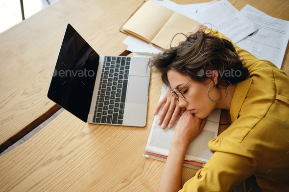 Top view of young tired woman dreamy fall asleep on desk with laptop and documents at workplace