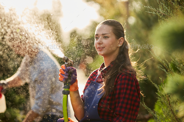 Work in the garden. Girl gardener sprays water and a guy sprays fertilizer on plants in the