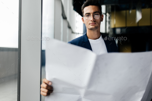 Architect in stylish clothes holds sheet with drawing in his hand and talks by phone on the - Stock Photo - Images
