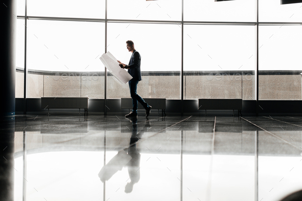 Architect in stylish clothes holds sheet with drawing in his hand and talks by phone on the - Stock Photo - Images