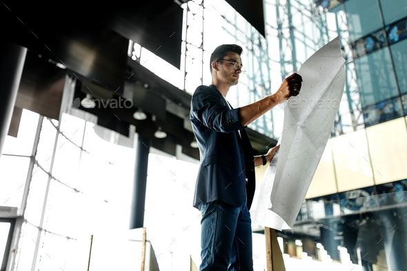 Architect in stylish clothes holds sheet with drawing in his hand and talks by phone on the