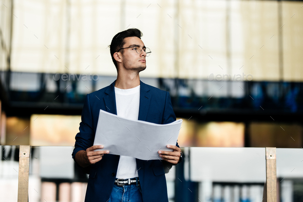 Architect in stylish clothes holds sheet with drawing in his hands on the  background of a modern Stock Photo by leikapro
