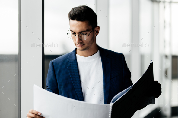 Architect dressed in stylish clothes stands next to window and explores the sheet with drawing in
