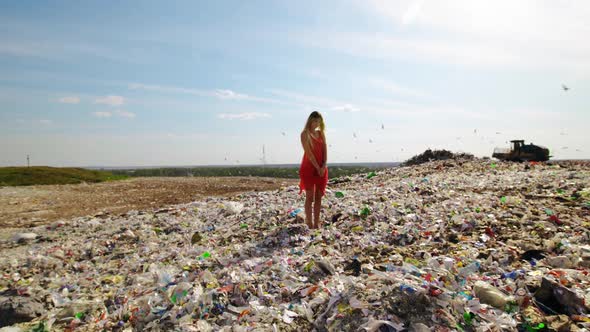 Epic Dolly in Young Woman in Red Dress Standing at Huge Trash Dump with Many Seagulls in Background alt