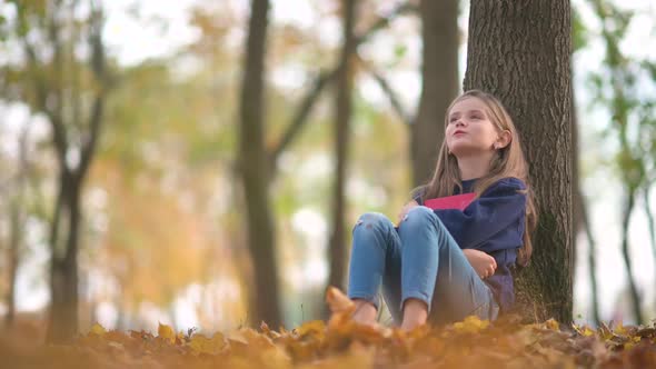 Cute Girl Reading A Book Sitting Under A Big Tree. alt