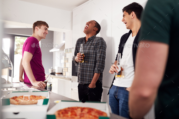 Group Of Male College Students In Shared House Kitchen Drinking Beer And Eating Pizza Together