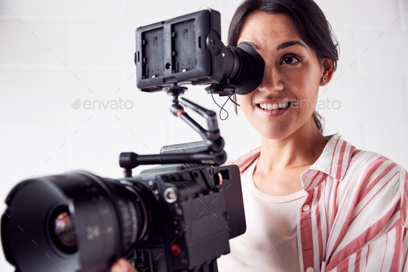 Female Videographer With Video Camera Filming Movie In White Studio