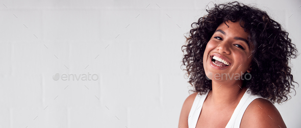 Portrait Of Smiling Casually Dressed Woman In Vest Top Standing Against White Brick Studio Wall