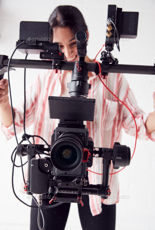 Female Videographer With Video Camera On Steady Cam Rig Filming Movie In White Studio