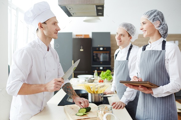 Positive young intern cooks asking chef at master class - Stock Photo - Images