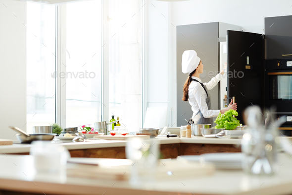 Female chef in hat opening refrigerator