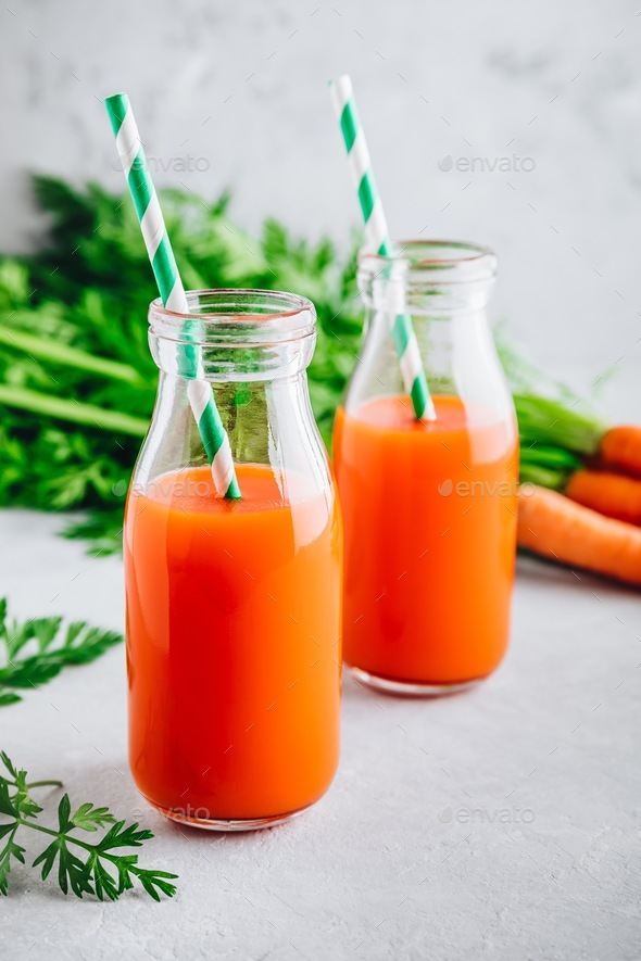 Fresh detox carrot juice in glass bottles on a gray stone
