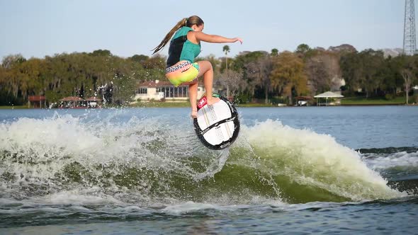 A young woman wake surfing behind a boat on a lake. alt