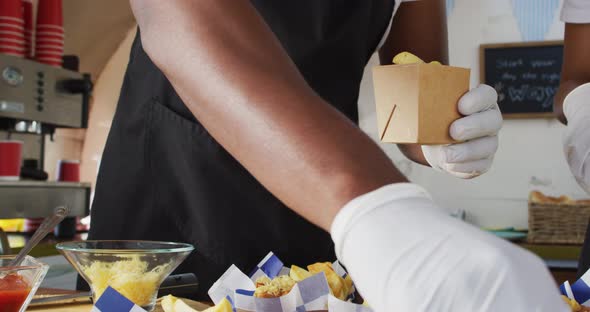 Mid section of african american man wearing apron putting fries in a box in the food truck alt