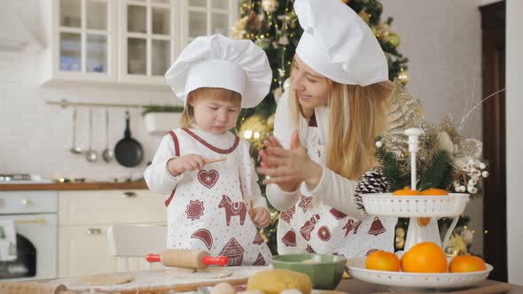 A Little Daughter and Her Mother Together Prepare Festive Cookies in the Kitchen in Chef's Hats