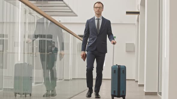 Man in Suit with Suitcase Walking along Airport alt