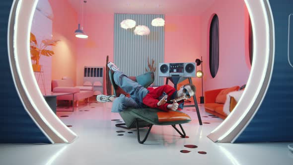 Expressive Hipster Man Lying on Armchair and Voguing in Vintage Studio alt