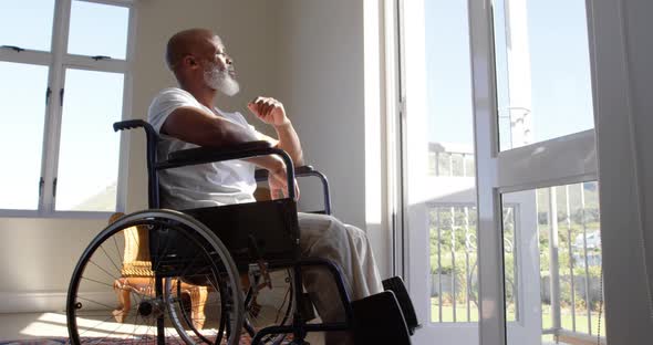 Side view of mature black handicap man sitting on wheelchair near the window at home 4k alt