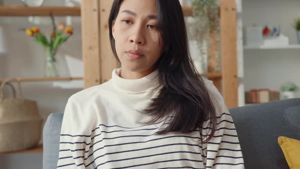 Asia lady sit embracing knees at sofa in living room at house look outside with feel lonely.