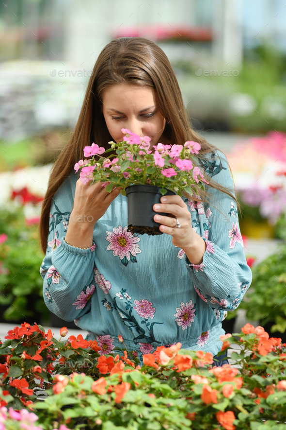 Woman in long sleeve shirt smelling pink flowers