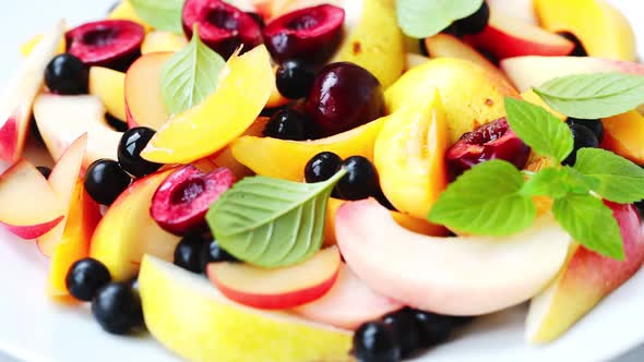 Fruit salad with berries in white plate, white background.  alt