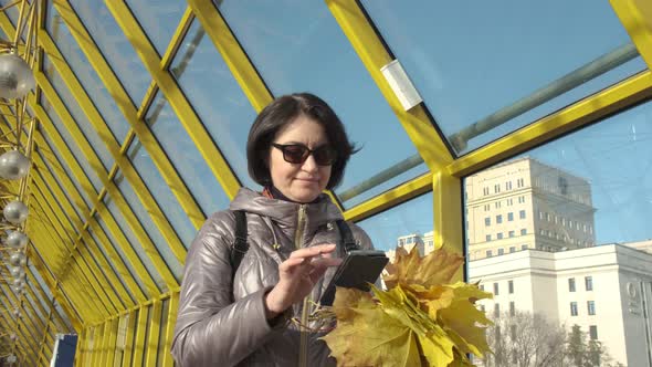 A Middleaged Woman Brunette Caucasian with Short Hair with a Bouquet of Yellow Leaves Walks Along alt