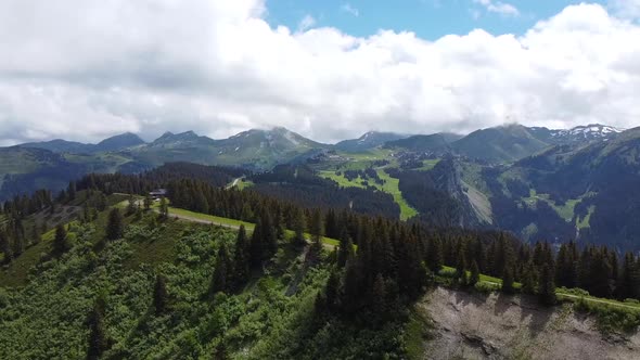 Drone Shot (rotating) of a Pine Tree-covered Crest with Mountains in the Background and a Cloudy but alt