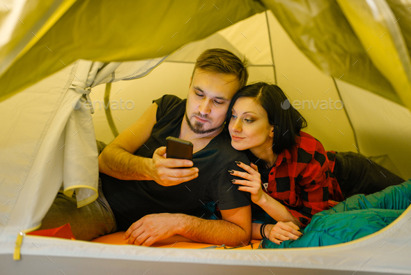 Couple with phone lying in tourist tent