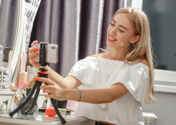 Pretty girl blogger sets the phone on the stand on the dressing table for shooting video for her