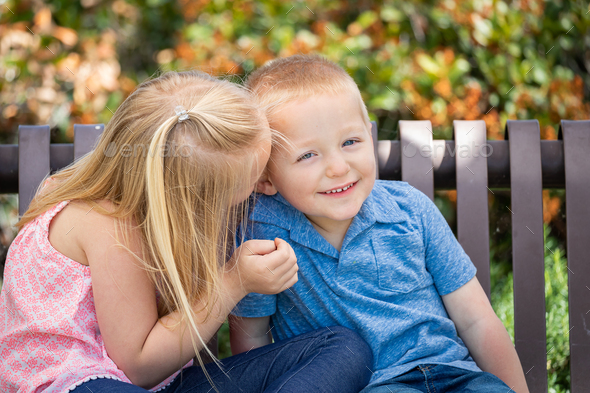 Young Sister and Brother Whispering Secrets On The Bench At The Park. - Stock Photo - Images