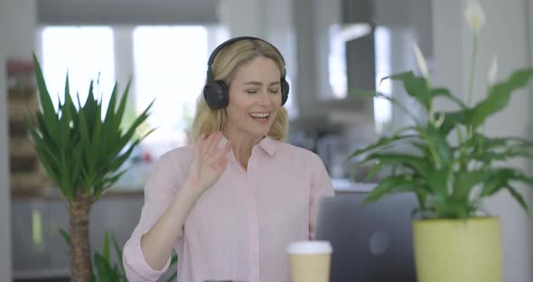 Blond woman with headphones making video call on laptop