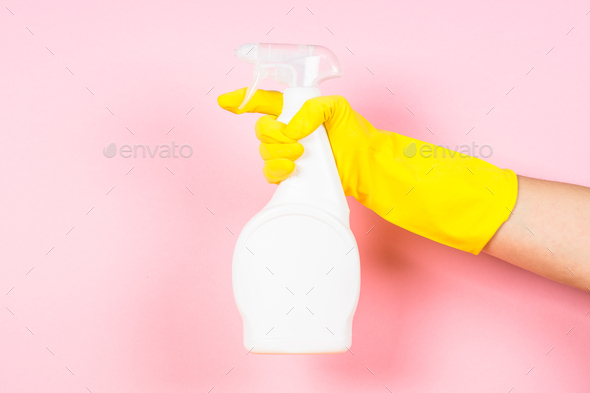 Hand in yellow gloves hold cleaning agent bottle on pink background