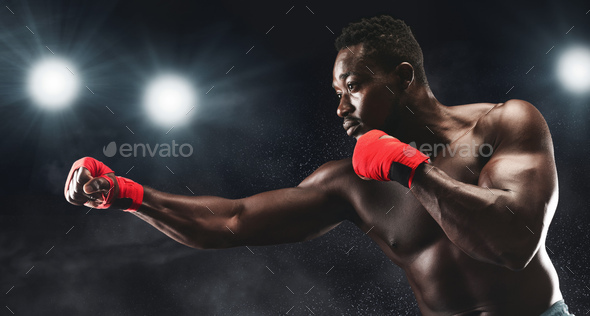 Side view of professional black man fighting on boxing arena