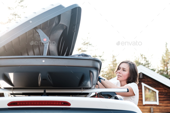 Satisfied woman puts things in the roof rack of the car or in the cargo box